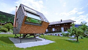 A modern house with a sloped roof and large windows, situated on a grassy area with a wooden building in the background. - Experience the special (Nußdorf/Debant)