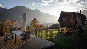 A modern outdoor seating area with a table and chairs, a unique building structure, and a mountainous backdrop. - Experience the special (Nußdorf/Debant)