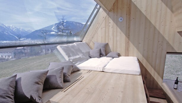 A cozy wooden interior with a bed and seating area, large windows offering a mountain view. - Experience the special (Nußdorf/Debant)