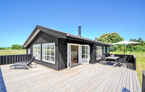 A modern wooden cabin with a deck, a patio area with a table and chairs, and a large open door leading to an interior space. - 3 bedroom lovely home in Grenaa (Grenaa)
