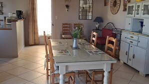 Un comedor con una mesa de vidrio, sillas de madera, un jarrón con flores y una zona de cocina con armarios y un microondas.