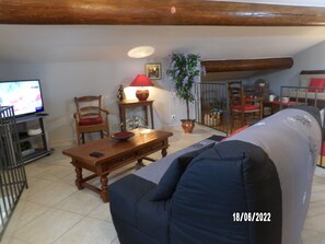 A living room with a wooden table, a blue sofa, a red lamp, and a television on the left.