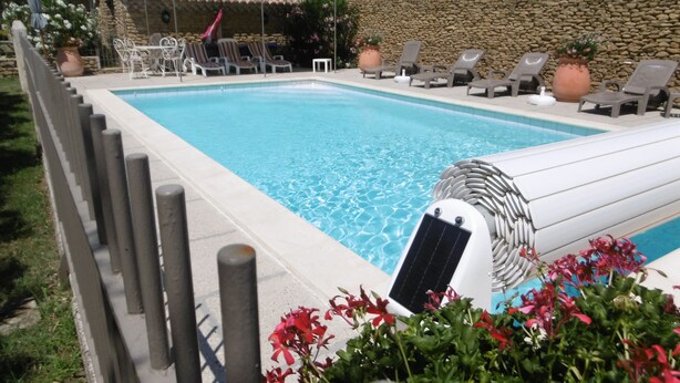 Una piscina con sillones de descanso y un muro de piedra al fondo.