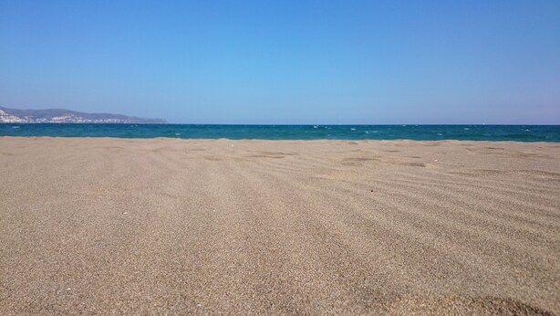 A wide sandy beach with a clear blue sky and calm sea.