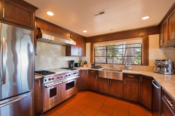 A modern kitchen with stainless steel appliances, wooden cabinets, and a large window providing natural light.