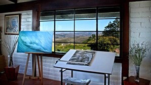 An art studio with an easel, a large window with a scenic view, and a framed painting on the wall.