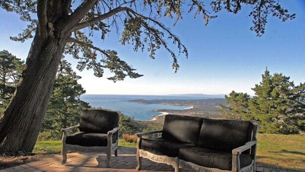 A bench and a sofa set on a brick patio overlooking a coastal landscape.