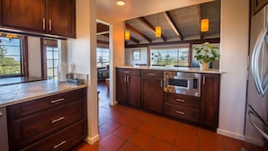 A modern kitchen with dark wood cabinets, stainless steel appliances, and large windows.