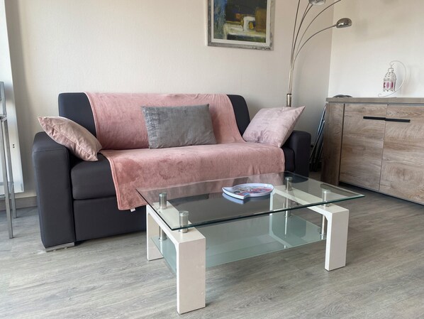 A modern living room with a glass coffee table, a black and pink sofa, and a wooden cabinet.