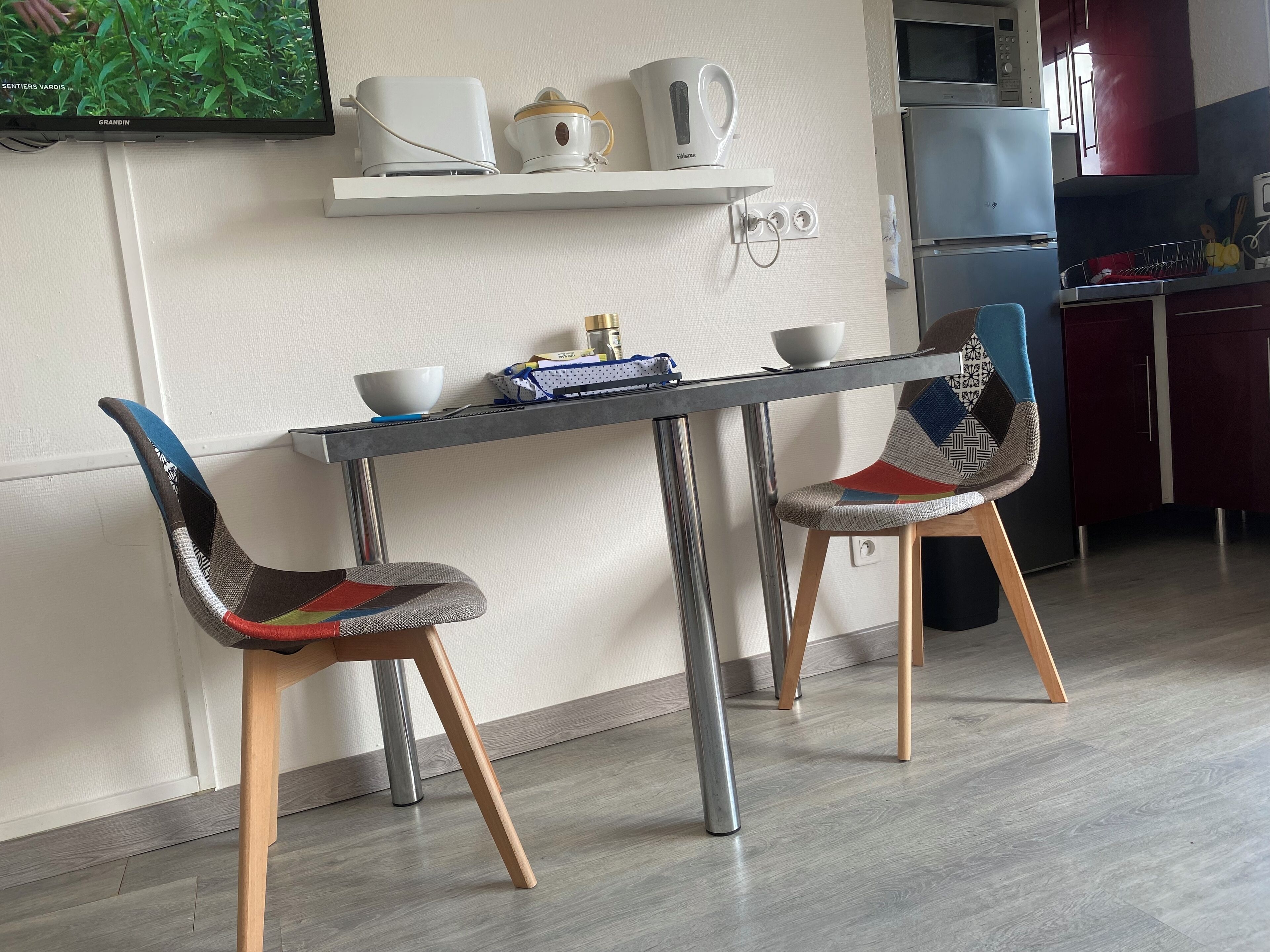 Une cuisine moderne avec une table à manger, deux chaises, un téléviseur fixé au mur et un four à micro-ondes.