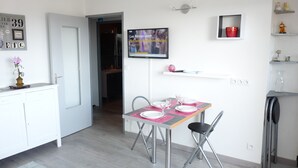 Een moderne keuken met witte kastjes, een eettafel voor vier personen en een aan de muur bevestigde televisie die een nieuwskanaal toont.