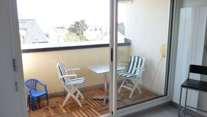 Een balkon met twee gestreepte stoelen, een kleine tafel, een blauwe plastic stoel en een houten vloer.