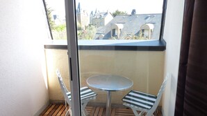 Een klein balkon met een ronde tafel en twee gestreepte stoelen, met uitzicht op een woongebied met verschillende architectuurstijlen.