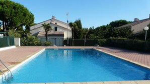 Piscina rectangular con solárium empedrado, rodeada por una valla y follaje.