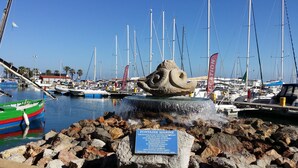 Un puerto deportivo con barcos, una gran escultura rocosa y un cartel con nombres.