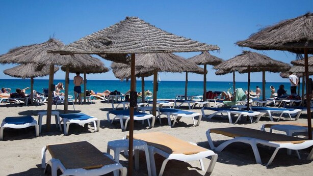 Una playa con sombrillas de paja y tumbonas.