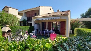 Una villa con un patio, una zona de estar cubierta al aire libre y un jardín con setos bien cuidados.