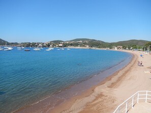 Uma praia costeira com águas azuis cristalinas, barcos e areal arenoso.