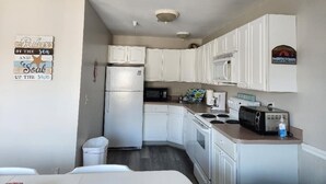 Una cocina compacta con armarios blancos, un refrigerador, un microondas y una pequeña encimera con un tostador y una botella de agua.