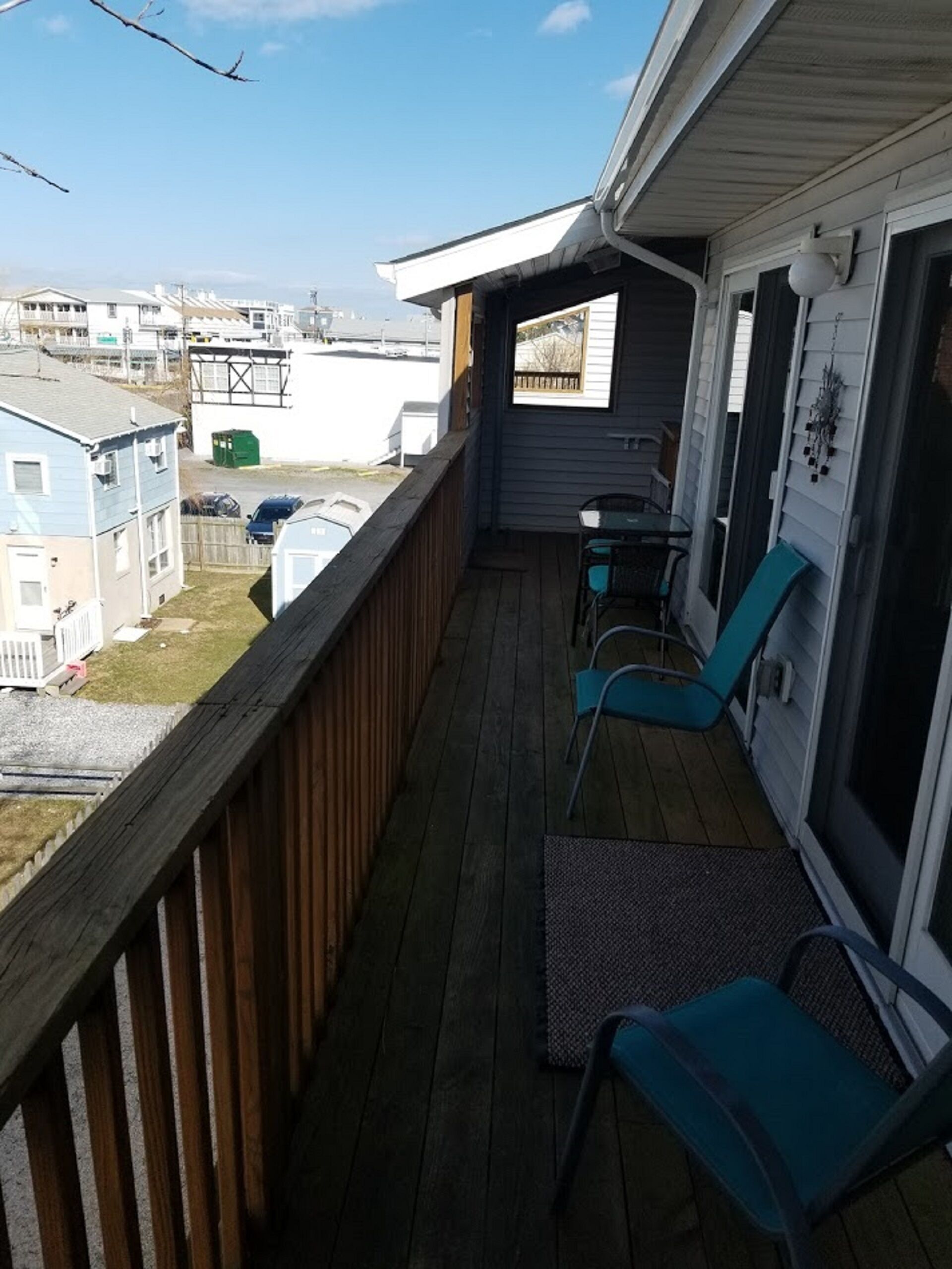Terraza de madera con dos sillas y una mesa, con vista a un barrio residencial.