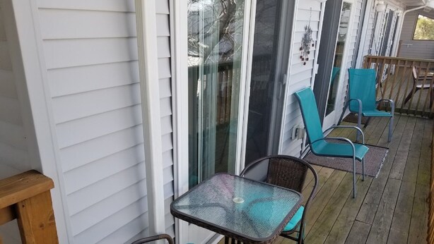 Un patio techado al aire libre con mesa y sillas de vidrio, cubierta de madera y puertas corredizas de cristal.