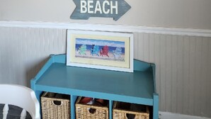Pared decorada con una pintura de playa, un letrero que dice 'BEACH' y una foto enmarco de sillas de playa sobre un estante azul.