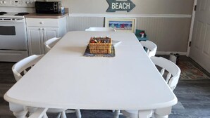 Un comedor con una mesa y sillas blancas, un microondas y un tostador en la encimera. Un cartel en la pared dice "BEACH".