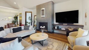 A modern living room with a large flat-screen TV, a fireplace, and a cozy seating area with a sofa and armchairs. - Modernist Mountain View Retreat in Old Mill!! Hot Tub!!!  Pool Table!!! (Bend)