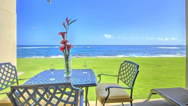 Mesa com um vaso de flores e dois copos, com vista para o oceano.