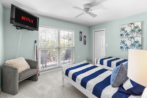 Un dormitorio con cama, una silla, televisor montado en la pared y ventilador de techo.