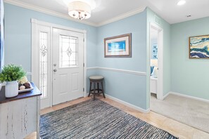 A hallway with a white door, a framed picture on the wall, and a small stool.