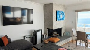 Ein modernes Wohnzimmer mit Kamin, Flachbildfernseher und Blick aufs Meer.