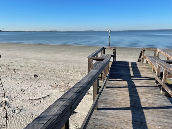 A wooden boardwalk leading to a sandy beach with calm water in the background.