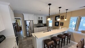 Una cocina moderna con armarios blancos, un refrigerador de acero inoxidable, una isla central con taburetes de bar e iluminación colgante.