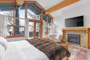 A bedroom with a large bed, a fireplace, a television, and large windows with curtains.