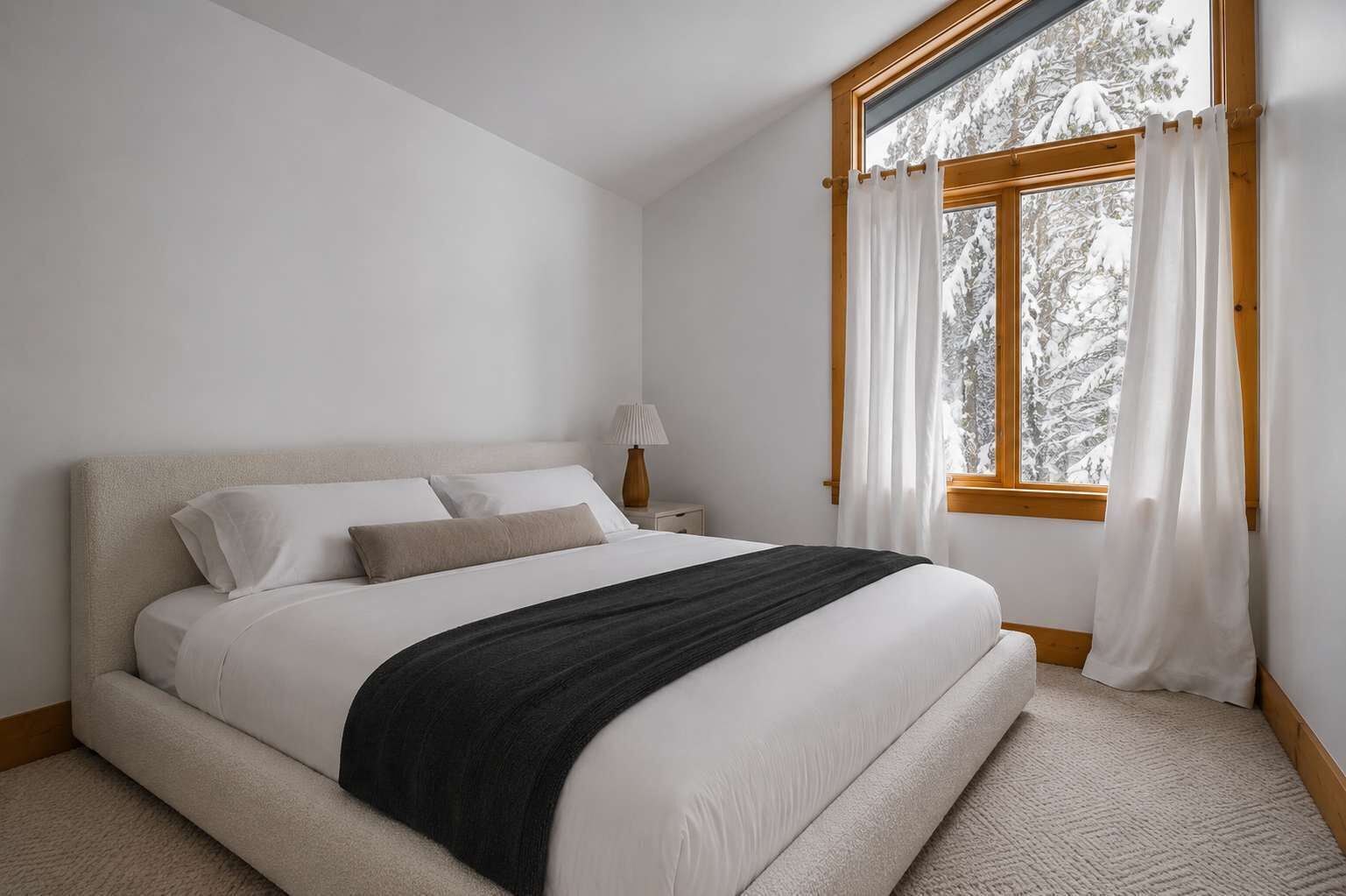 A bedroom with a bed, a nightstand, a lamp, and a window with curtains.