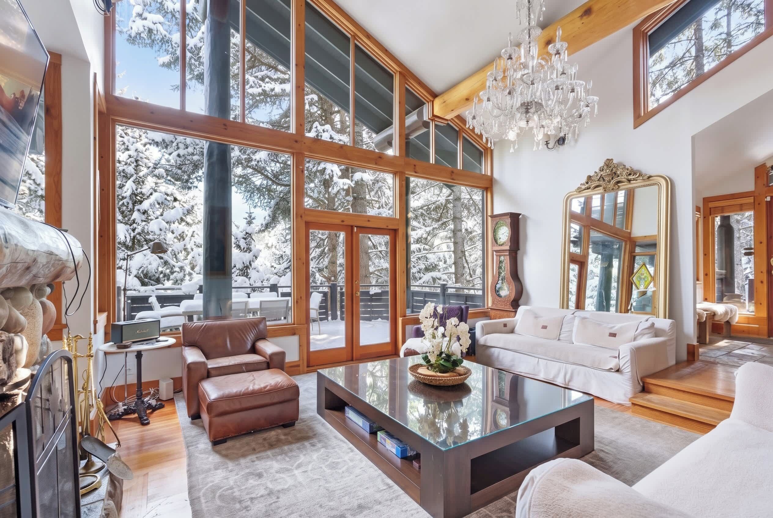 A spacious living room with large windows, a chandelier, and a fireplace.