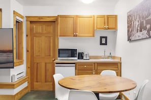 A compact kitchen with wooden cabinets, a microwave, a coffee maker, and a sink. There is a round wooden table with chairs.