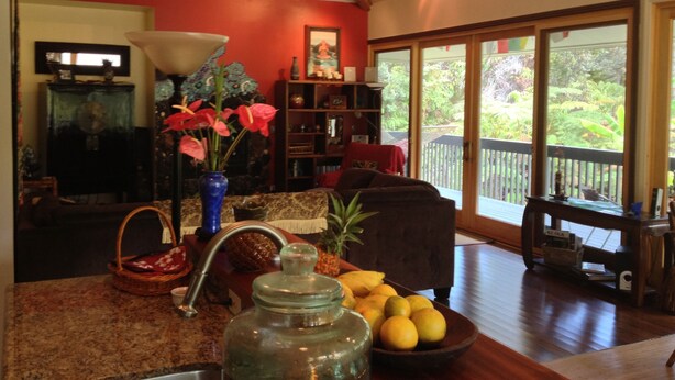 A living room with a wooden coffee table, a vase with flowers, a bowl of fruit, and a bookshelf. - ~Peace and Tranquility in rain-forested Volcano on luxurious property ~ (Volcano)