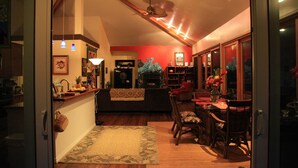 An open-plan living area with a dining table, chairs, and a kitchen area visible through an open doorway. - ~Peace and Tranquility in rain-forested Volcano on luxurious property ~ (Volcano)