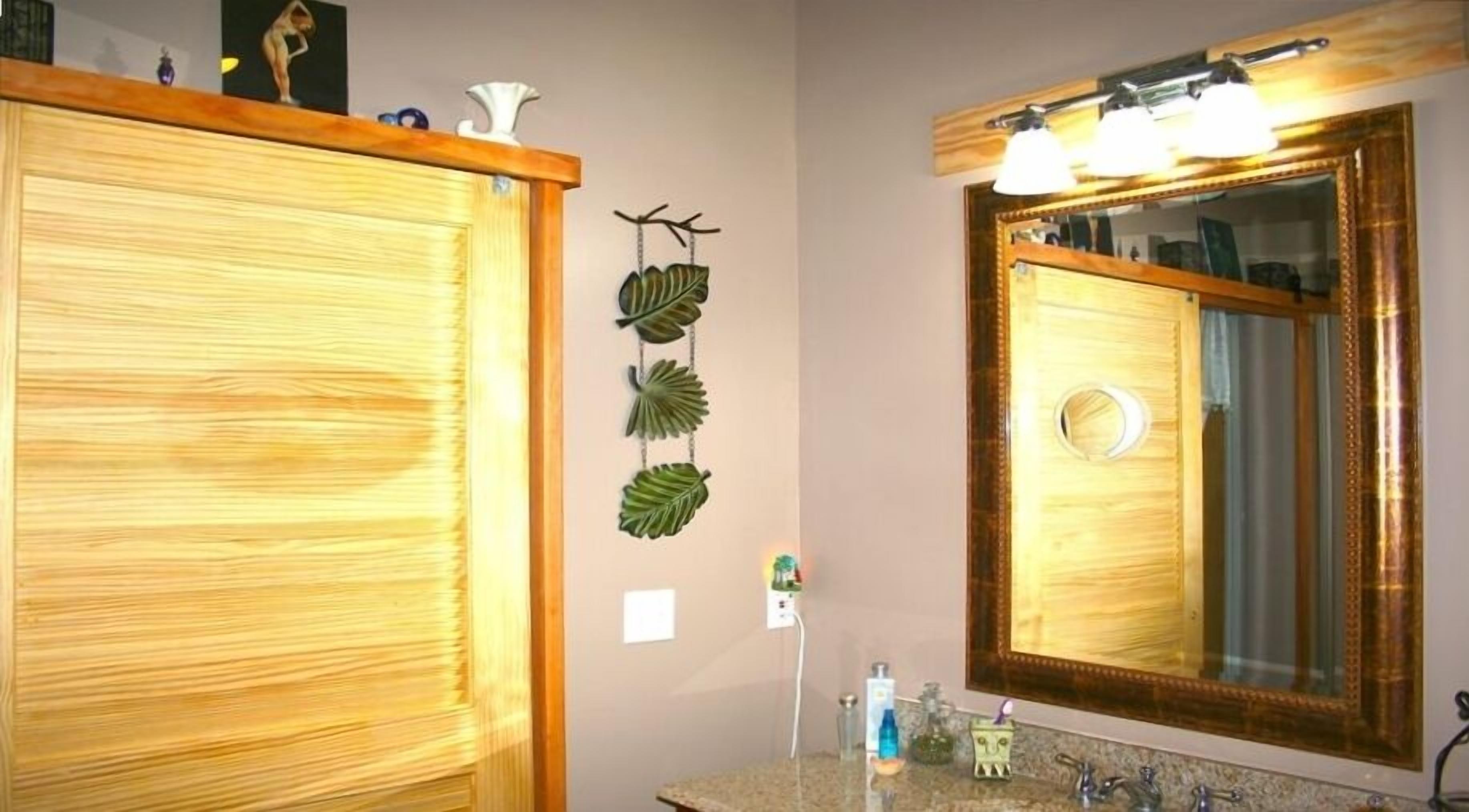 A bathroom with wooden cabinets, a mirror with lights, and a plant decoration.