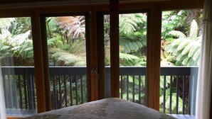 A bedroom with a bed, wooden balcony doors, and a view of lush green ferns. - ~Peace and Tranquility in rain-forested Volcano on luxurious property ~ (Volcano)