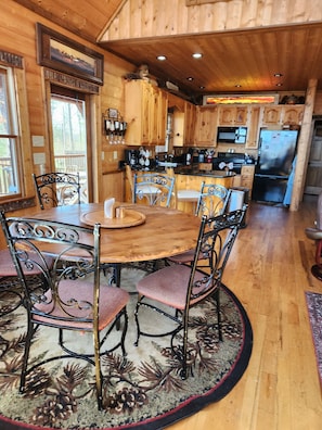 A wooden cabin interior with a round dining table, metal chairs, and a kitchen area with wooden cabinets and appliances. - 3 King Suites! Great Views! Outdoor Fireplace! Paved Roads! Pets! Access Ramp! (Blue Ridge)