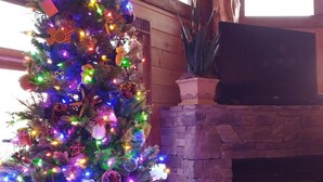 A Christmas tree with multicolored lights in a room with a stone fireplace and a leather chair. - 3 King Suites! Great Views! Outdoor Fireplace! Paved Roads! Pets! Access Ramp! (Blue Ridge)