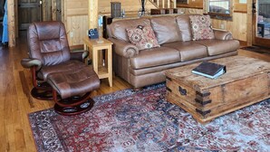 A spacious wooden cabin interior with a high ceiling, a wooden staircase, a leather sofa, a leather armchair, a small table, and a patterned rug. - 3 King Suites! Great Views! Outdoor Fireplace! Paved Roads! Pets! Access Ramp! (Blue Ridge)