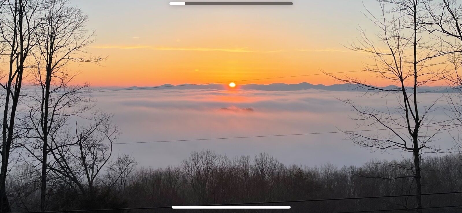 A sunrise over a mountainous landscape with trees in the foreground.