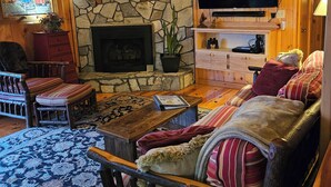 A cozy living room with a stone fireplace, wooden furniture, and a flat-screen TV mounted above it. - Two King Suites! Endless View!  Close to Town. All paved roads. Pet Friendly. (Blue Ridge)