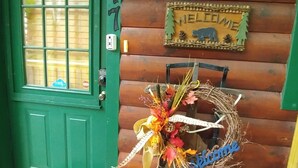 A wooden cabin with a green door, a welcome sign, and a wreath on a bench. - Two King Suites! Endless View!  Close to Town. All paved roads. Pet Friendly. (Blue Ridge)