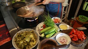 Una cocina con varias verduras, un wok sobre la hornilla y una persona cocinando.