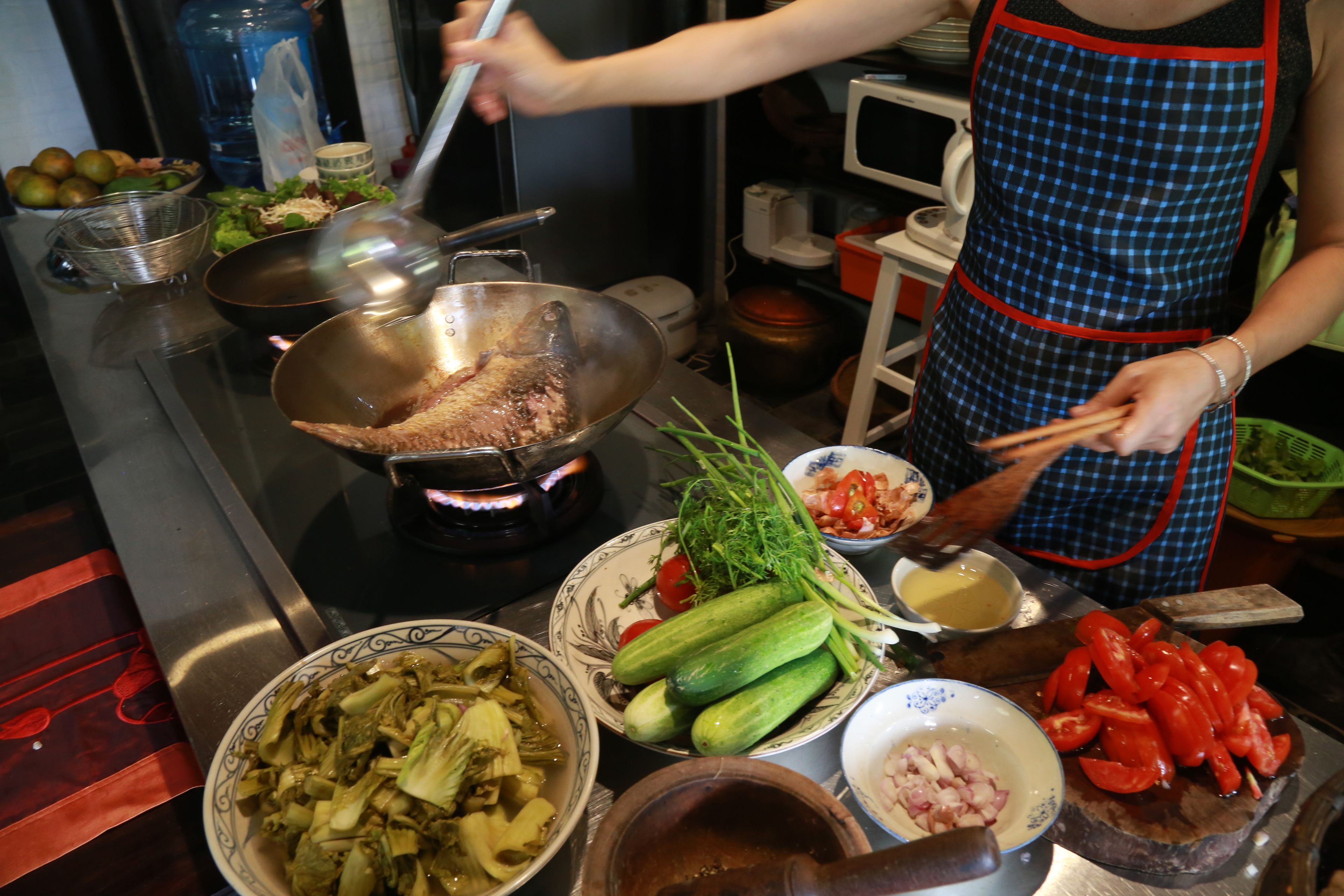 A kitchen with a stove, cooking utensils, and various vegetables.